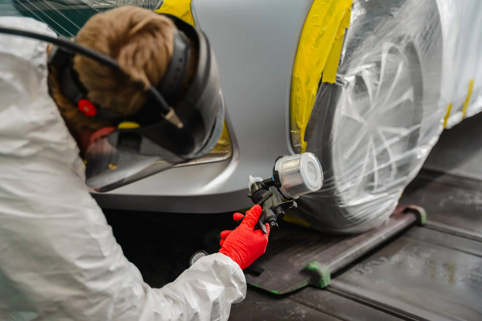 AutoLux employee preparing and spraying a car body panel